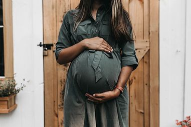 A pregnancy woman holding her belly standing outside in front of a wooden door.